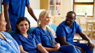 Keski-Suomen hyvinvointialueen hymyileviä työntekijöitä istuu sohvalla. Sohvan takana seisoo yksi työntekijä.