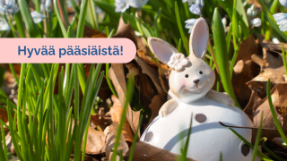 Pääsiäispupukoriste istuu maasta pilkottavien kukanvarsien seassa. Kuvassa on teksti 'Hyvää pääsiäistä!'.   