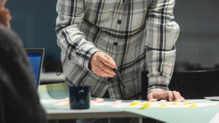 Henkilö työskentelemässä työpöydän ääressä kynä kädessään.