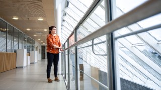 Nainen katselee lasiseinän läpi ulos käytävän kaiteen vierellä.