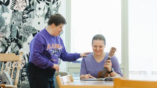 Yksi henkilö soittaa ukulelea ja toinen henkilö laulaa.