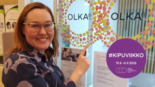 Nainen osoittaa lasiseinää, jossa lukee teksti 'OLKA'. Violetissä ympyrässä teksti: 'Kipuviikko'. 