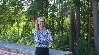 Tiina Föhr seisoo hymyilevänä Jyväskylän yliopiston kampuksella vehreän metsän ja aidan vieressä.